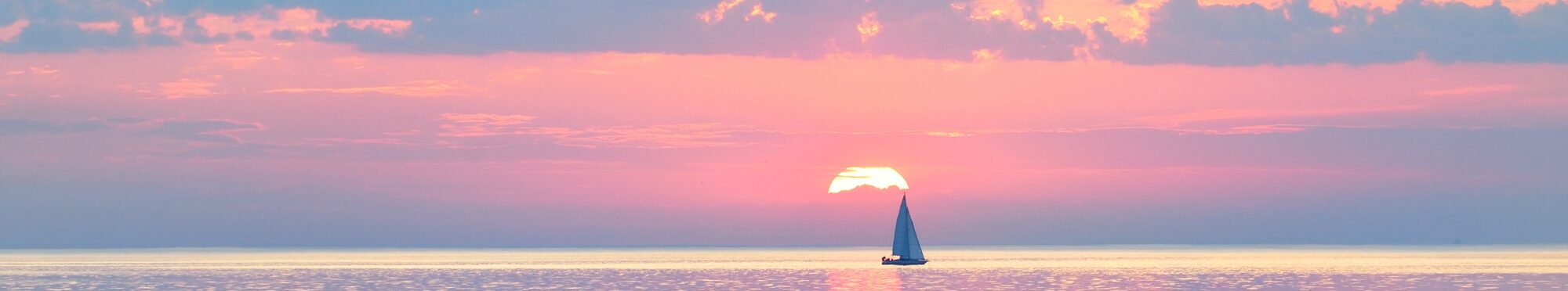Sloop rigged yacht sailing in an open Baltic sea at sunset. Colorful evening sky. Stunning seascape