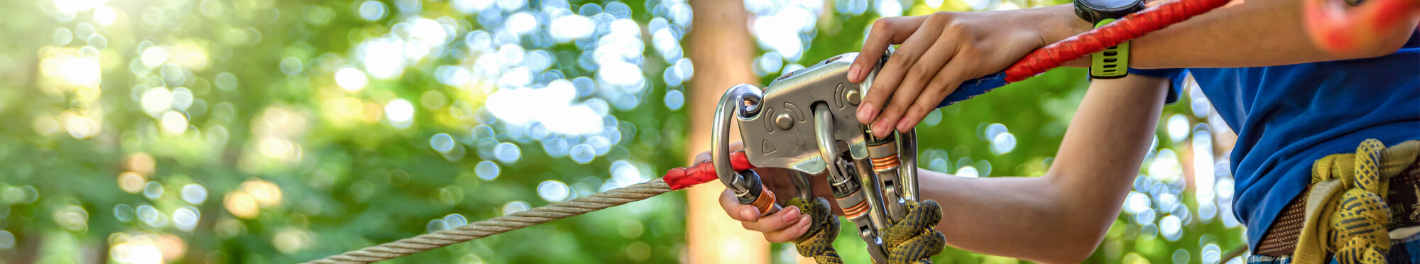Woman hangs a carabiner on a rope in a forest adventure park. Using climbing equipment: carabiner, belt, rope. Banner for advertising, design or website header