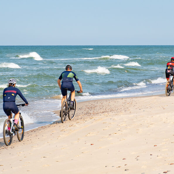 Cyclists with bikes riding on a beautiful sandy beach with rough Baltic Sea on background